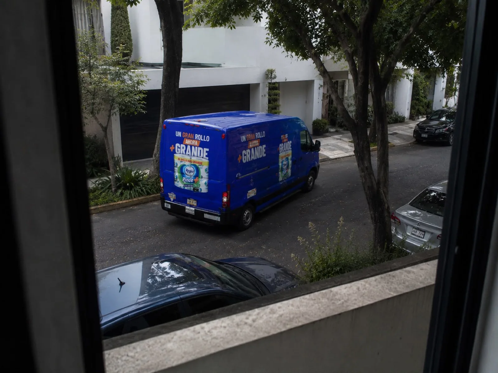 Delivery van with Regio advertising driving down a residential street, seen from a house window